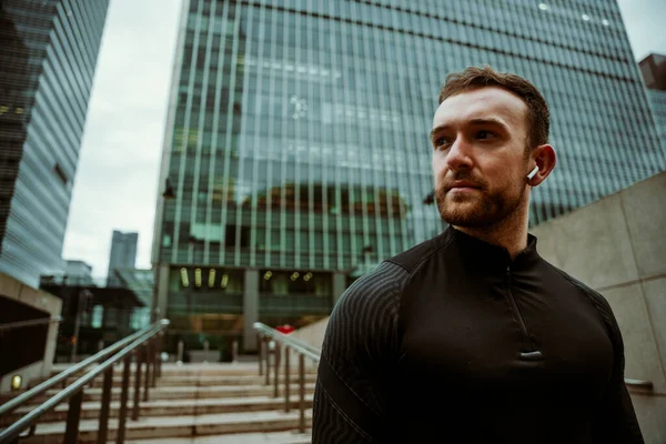 Handsome male athlete walking through city taking a break from outdoor run listening to music