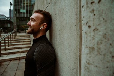 Beyaz erkek sporcu, şehir dışında koşuya çıkıp kulaklıkla müzik dinliyor.