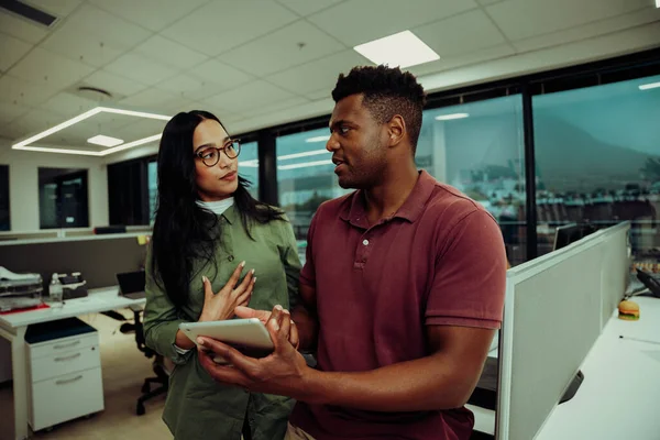 Due partner multietnici discutono questioni mentre tengono il tablet digitale in piedi nello spazio ufficio — Foto Stock