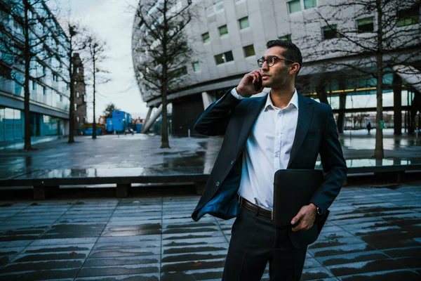 Uomo d'affari di razza mista che indossa tuta parlare sul dispositivo cellulare al di fuori dell'edificio degli uffici — Foto Stock