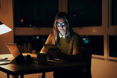 Beyaz iş kadını ofis masasında çalışıyor. İş raporuyla meşgul. Dijital tablette e-postaları okuyor. 