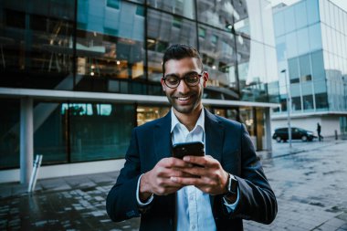 Gülümseyen karışık ırk işadamı. Akıllı telefondan mesaj atıyor. Ofise giderken yolda yürüyor. 