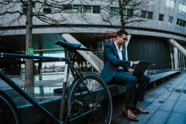 Melez yarış işadamı yemek molasında ofisin dışında oturmuş dizüstü bilgisayarla yazı yazıyor.