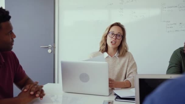 Diseñadora chateando con colegas de raza mixta investigando en laptop trabajando en proyecto de colaboración durante reunión matutina en oficina — Vídeo de stock