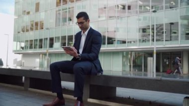 Karışık ırk işadamı tablette yazı yazıyor. Ofis binasının üstündeki balkonda oturuyor.