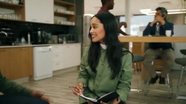 Genç melez kadın iş arkadaşlarıyla gülüyor ve yaklaşan proje hakkında sohbet ediyor ofis salonunda oturuyor.