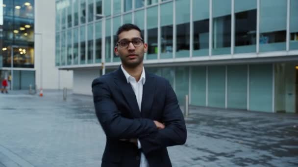 Бизнесмен смешанной расы улыбается стоя перед офисными зданиями — стоковое видео