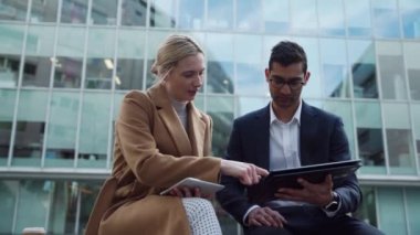 Karışık ırk işadamı ve Kafkas iş kadını dijital tablet üzerinde iş yerinin önündeki bankta oturuyorlar.