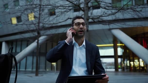Бизнесмен смешанной расы беседует с коллегами по смартфону, сидя в городе, заканчивая работу — стоковое видео