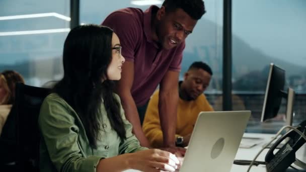 Змішана раса жіночий дизайнер досліджує ноутбук, тоді як етнічний колега-чоловік допомагає працювати в офісі — стокове відео