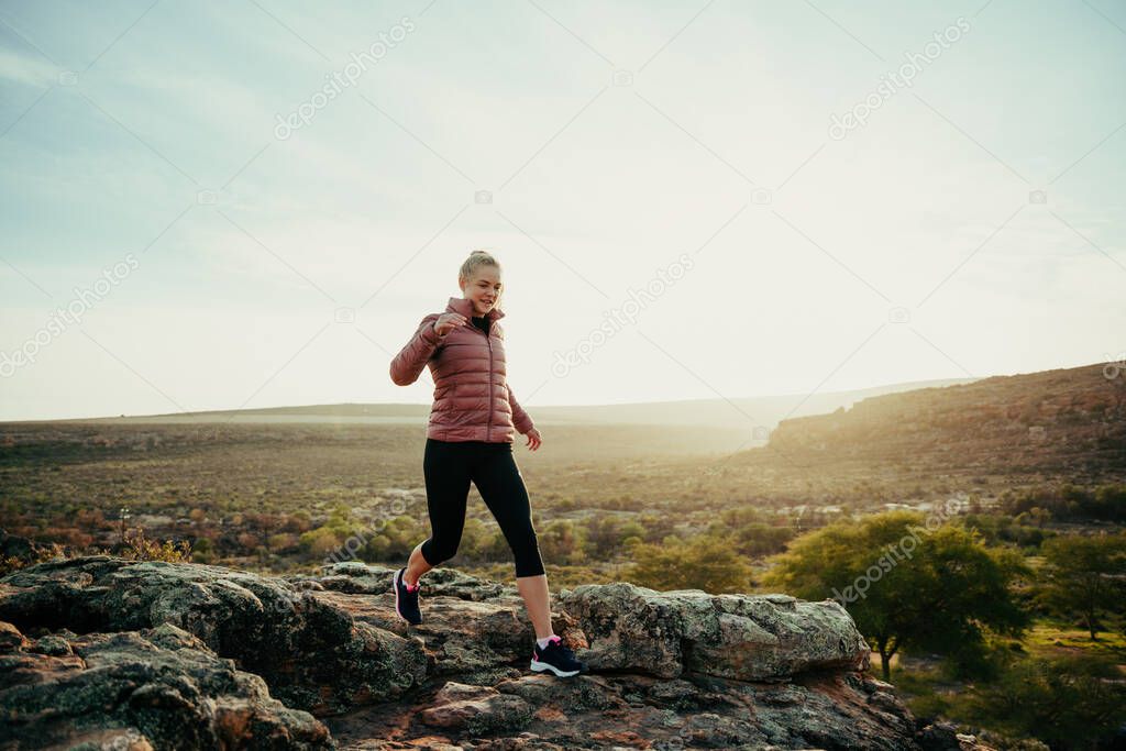 Caucasian female running in mountain along hiking trail skipping down rocks during sunset
