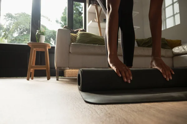 Jonge fit vrouw rollen yoga mat om te beginnen met oefenen in schone woonkamer. — Stockfoto
