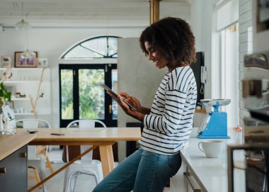 Genç bir kadın evdeki mutfakta internette geziniyor.