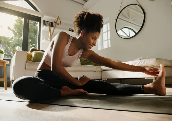 Mooie lachende vrouw stretching na lange yoga stroom zittend op yoga mat in moderne lounge — Stockfoto