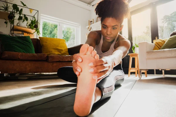 Young female working out from home and stretching legs on yoga mat