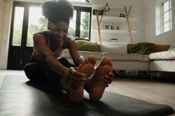 Yoğun sıcak yoga akışından sonra, geniş oturma odasındaki paspasın üzerinde uzanan gülümseyen kadın.