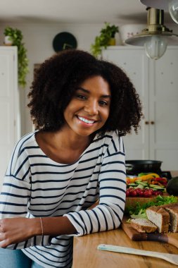 Güzel Afro-Amerikan kadın portresi tezgaha yaslanmış tasarımcı mutfağında sağlıklı sandviç yapıyor..