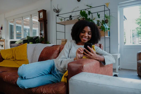 mixed race women happily scrolling through her phone while on the couch.