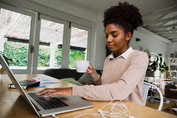Studente donna che fa appunti digitando sul computer portatile che tiene il caffè caldo seduto in cucina fantasia. — Foto Stock