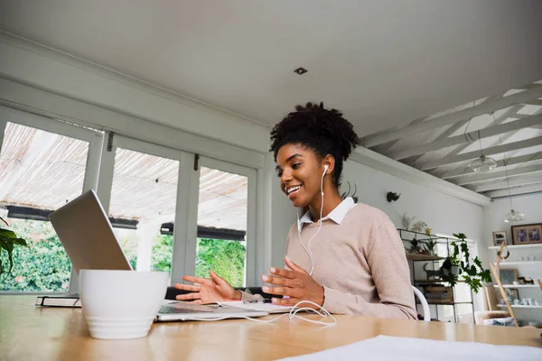 Donna d'affari sorridente che indossa auricolari che chiacchierano in videochiamata sul computer portatile con caffè in cucina moderna. — Foto Stock