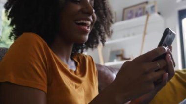 Genç melez kadın, arkadaşından mesaj alırken akıllı telefona gülüyor.