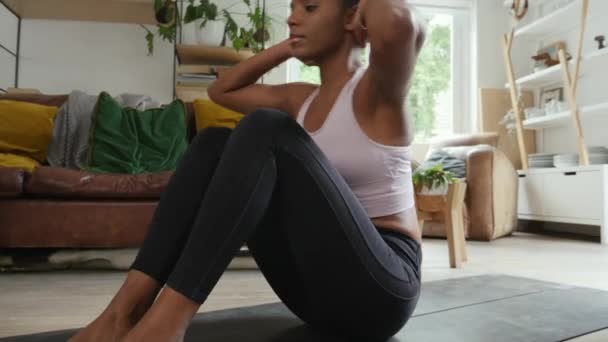 Молода спортсменка змішаної раси, яка працює з дому, роблячи ab чіпси в залі — стокове відео