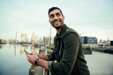 Hücresel cihazda yazan liman köprüsüne yaslanmış gülümseyen melez erkek. 