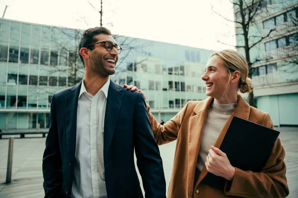 Uomo e donna d'affari caucasici che sorridono passeggiando per la città tenendo il taccuino — Foto Stock