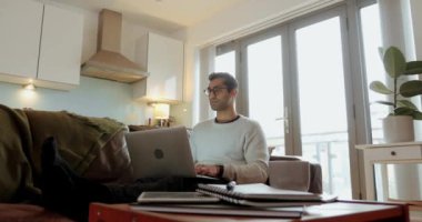 Karışık ırk işadamı evde çalışıyor dizüstü bilgisayarında oturuyor oturma odasında koltukta oturuyor.