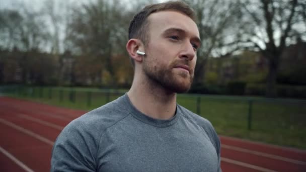Blanc athlète masculin emballant jusqu'à tenant sac à dos écouter de la musique avec écouteurs — Video