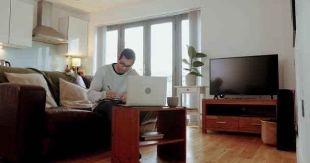 Carrera mixta hombre de negocios que trabaja en el ordenador portátil sentado en el sofá en la sala de estar — Vídeos de Stock