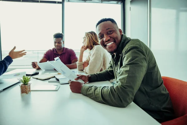 Mixed race business man smiling working through paperwork with parters sitting around table in conference room — 图库照片