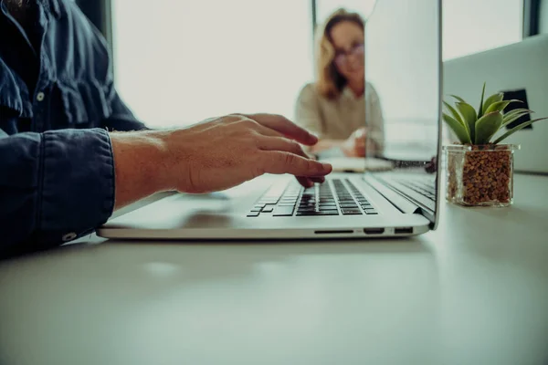 Close up of male caucasian business man typing on laptop while female worker smiling wearing glasses sitting in board room — 图库照片