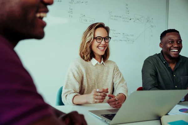 Kadın iş kadını, konferans sırasında masanın etrafında oturan meslektaşlarının sunduğu yeni proje fikirlerine gülüyor. 