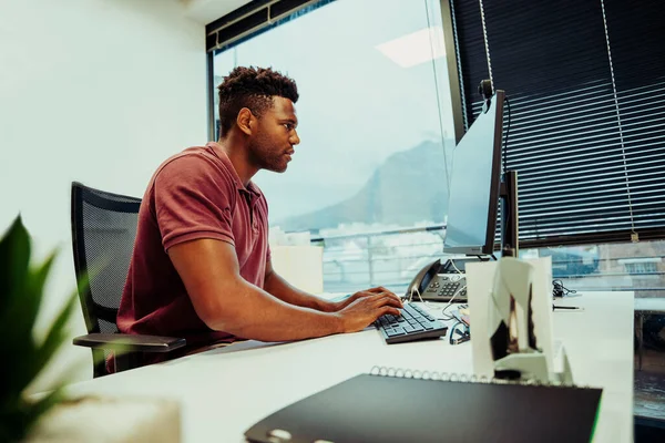 Imprenditore afroamericano di sesso maschile alla ricerca di disegni logo per l'azienda utilizzando computer portatile desktop seduto in ufficio fantasia — Foto Stock