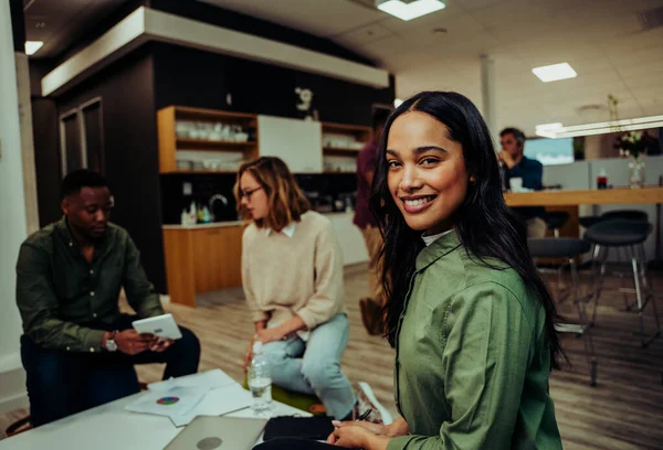Karışık ırk bayan yöneticisi gülümserken, meslektaşlar konferans salonunda iş görüşmesi hazırlıklarını tartışıyorlar. 