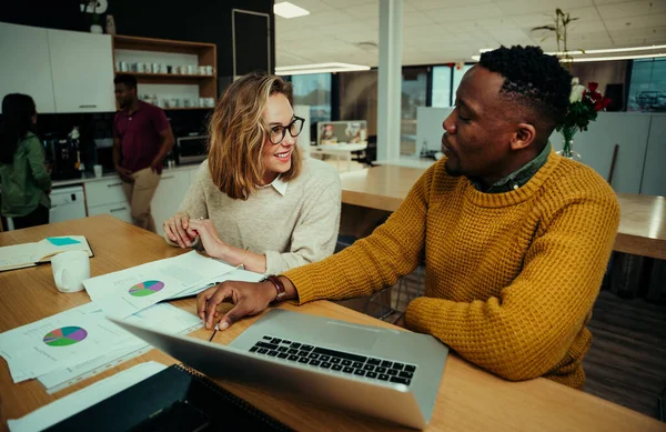 Ofiste çalışan genç girişimciler turta grafiklerini analiz ediyor ve iş arkadaşları bir fincan kahve içerken laptopta araştırma yapıyorlar.