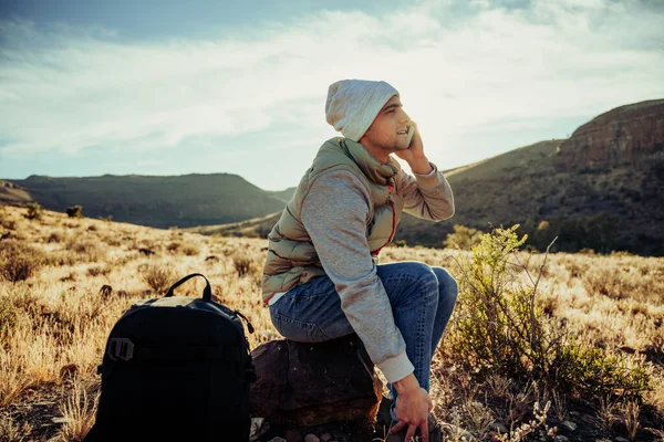 Young caucasian teenager chatting to friends while spending alone time hiking in mountain terrain — Stock Photo, Image