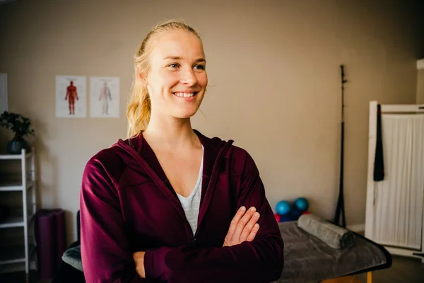 Mooie glimlachende fysiotherapeut gelukkig staande met gekruiste armen in pilates studio — Stockfoto