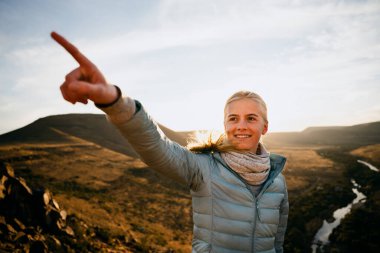 Genç beyaz kadın gün batımından sonra bir dağın tepesindeki güzel manzarayı işaret ediyor.