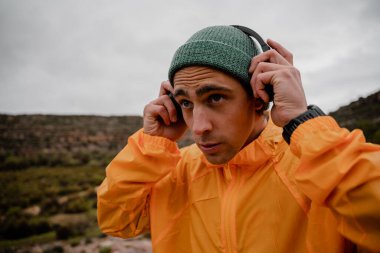 Odaklanmış genç erkek sporcu, bulutlu bir havada dağ yolunda koşmadan önce akıllı telefondan müzik için kulaklık kullanıyor.