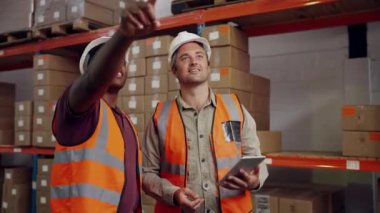 Meslektaşlar kontrol listesini düzelterek fabrika deposuna yeni gelen paketleri gösteriyorlar. Gülümsüyor ve birlikte çalışmaktan keyif alıyorlar.