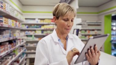 Eczanede palto giyen müşteriler için dijital tablet üzerinde ilaç bulan beyaz kadın doktor. 