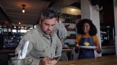 Güzel etnik garson modaya uygun kafede orta yaşlı erkek yumurtalı kahvaltı servisi yapıyor..