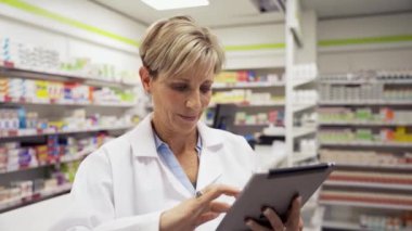 Kadın eczacı dijital tabletin ayarlarını düzeltirken, asistan da eczanenin arkasındaki senaryoları düzenliyor. 