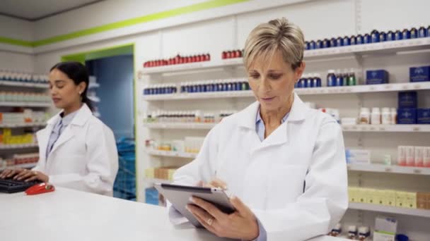 Caucasian pharmacist scrolling through scripts on digital tablet standing at counter in pharmacy. — Stock Video