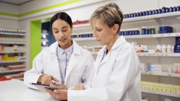 Female intern being assisted by caucasian pharmacist locating pills in pharmacy — Stock Video