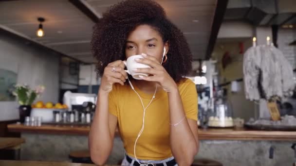 Piękna kobieta słuchając muzyki i trzymając kawę, siedzi w funky kawiarni. — Wideo stockowe