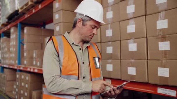 Travailleur caucasien tapant sur tablette numérique assortiment de colis selon check-list debout dans l'entrepôt d'usine — Video
