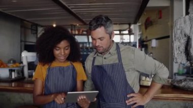 Güzel kafe sahipleri, önlük giyiyorlar, son moda kahve dükkanında dururken tablet üzerinde projeleri tartışıyorlar..